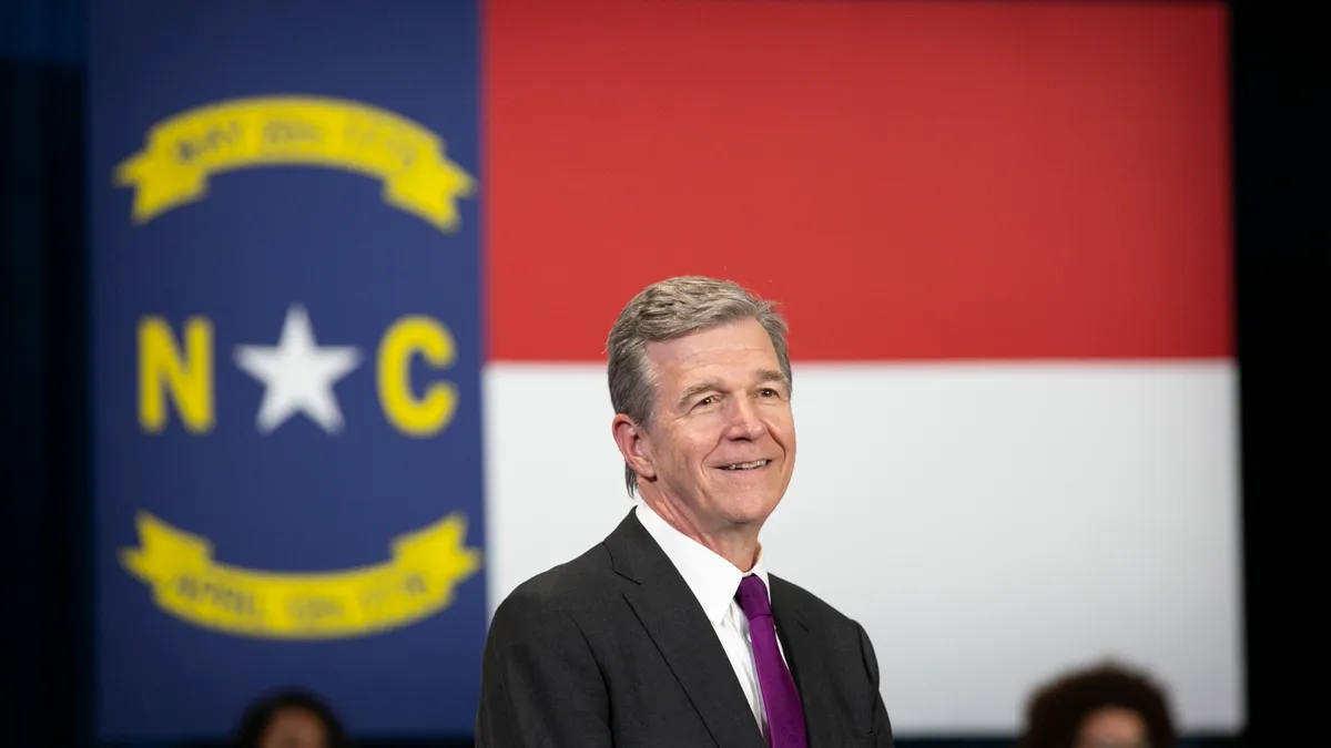 North Carolina Gov. Roy Cooper stands in front of a blurred state flag