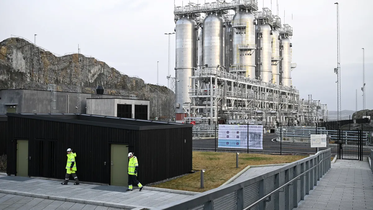 Two men walk in front of an industrial facility.