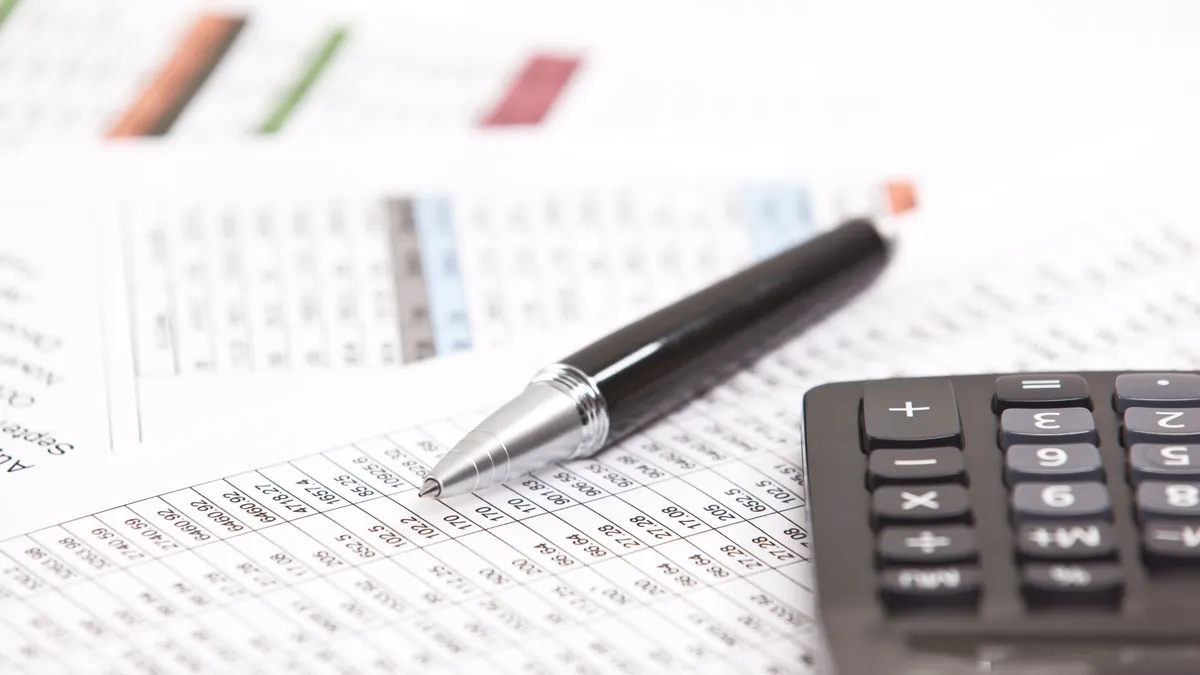 A photograph with a close up of a financial spreadsheet with a black caalculator on the right and a black pen in the middle.