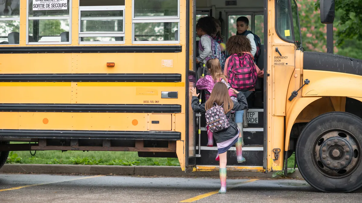 Kids wearing rain boots and backpacks run onto the school bus.