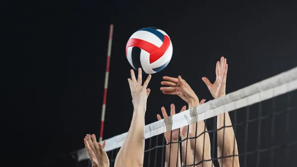 Several hands reach for a volleyball over a net.