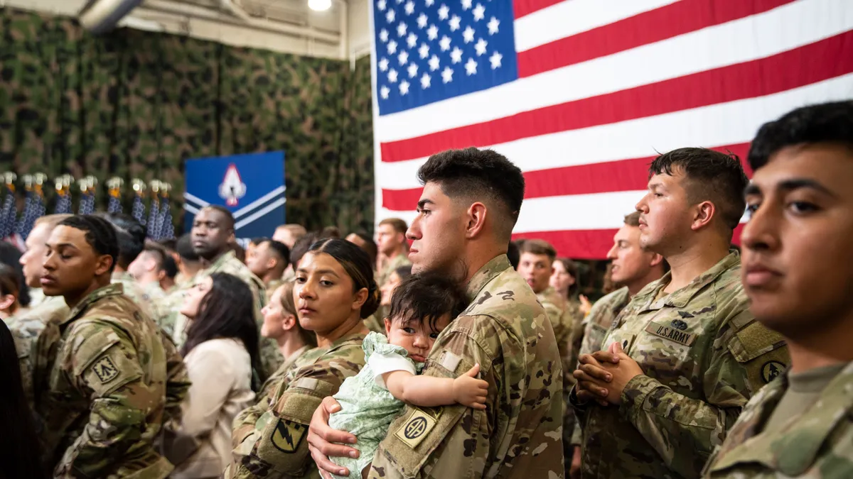 Military personnel and their families stand in their uniforms at an event in an auditorium.