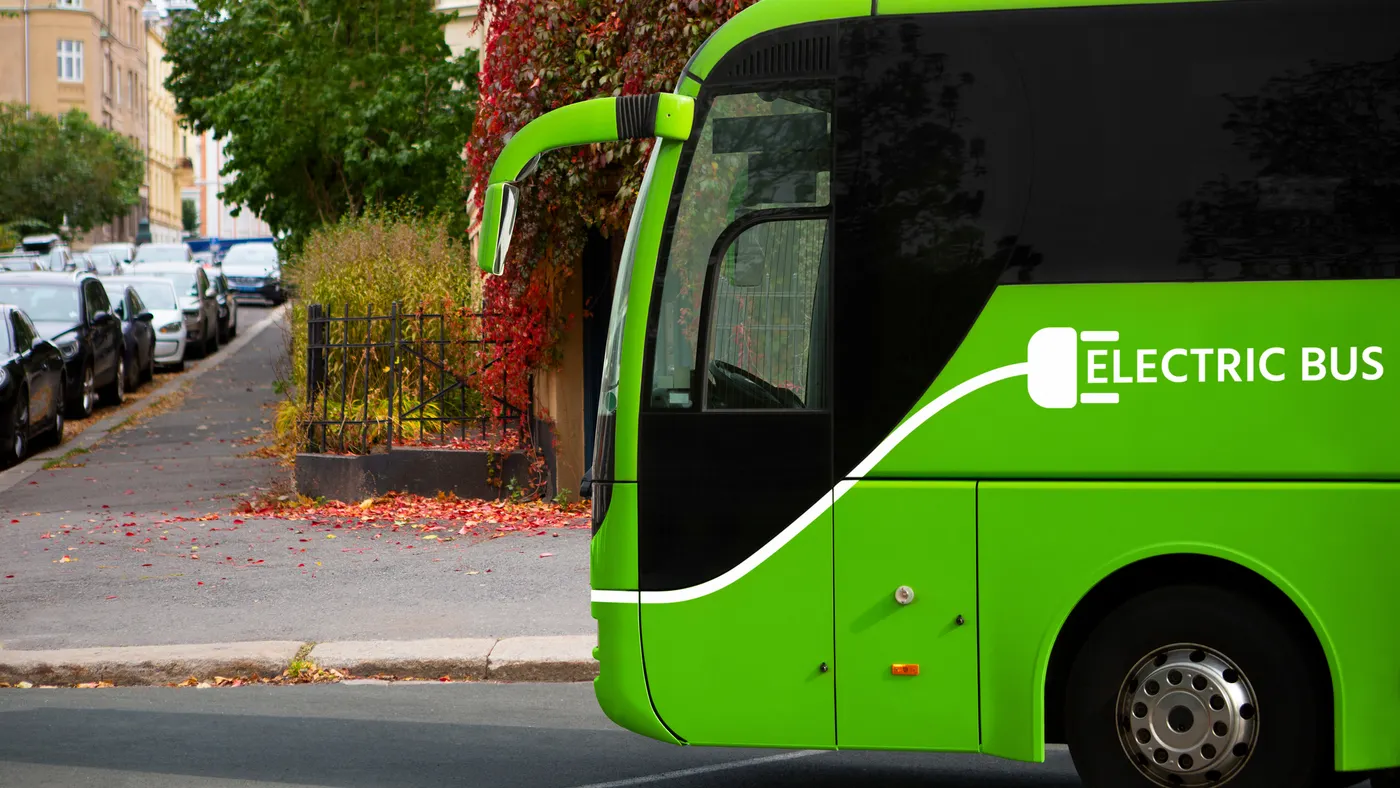 The left front of a green bus on a street is marked as "Electric Bus."