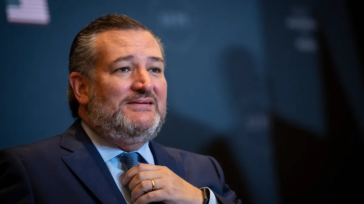 Sen. Ted Cruz, wearing a blue suit, adjusts his tie while he speaks.