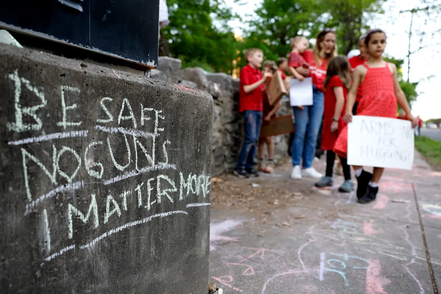 In the foreground is a chalkboard sign with anti-gun message. In the background are blurred images of children holding signs.