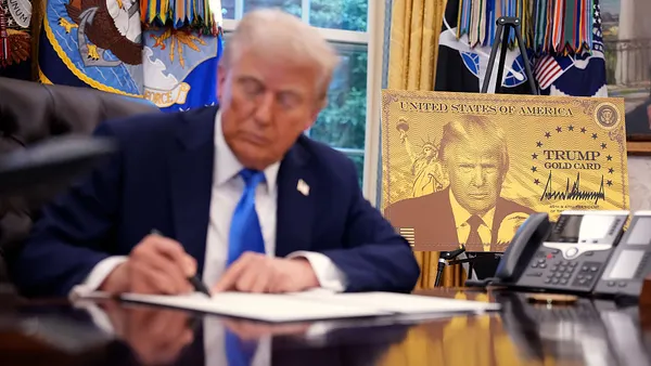 A poster of the "Trump Gold Card" is seen as President Donald Trump signs an executive order in the Oval Office at the White House on September 19, 2025 in Washington, DC.