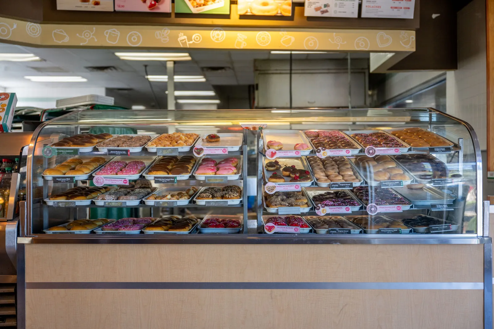 Doughnuts of various flavors and colors within a display case inside a Krispy Kreme shop.