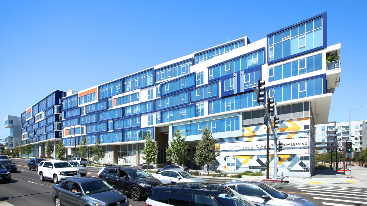 A blue, white and orange apartment building on a busy street.