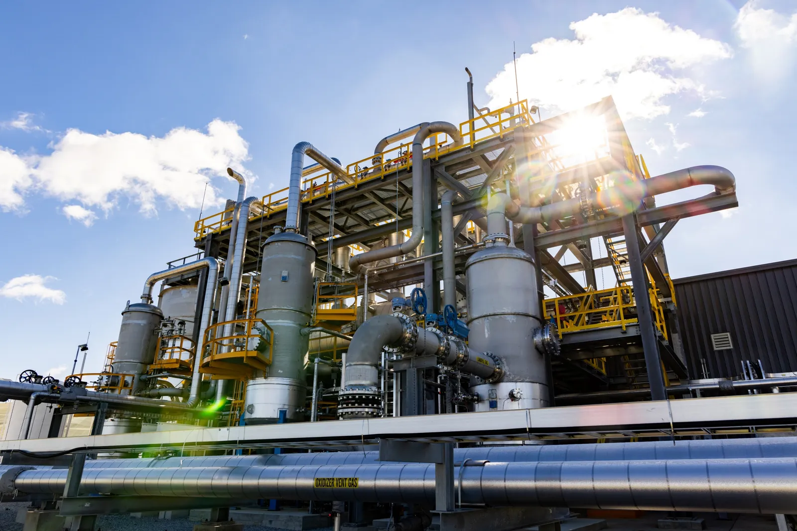 A large, complex system of metal pipes and boilers sits outside on a sunny day.