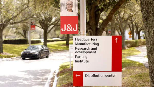 A car drives down a road lined with trees toward a sign that reads "Headquarters Manufacturing Research and development Parking Institute Distribution center."