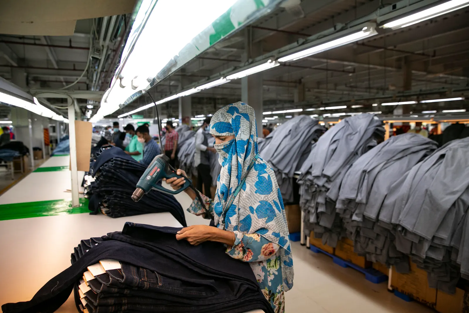 Workers in a line complete work on piles of pants.