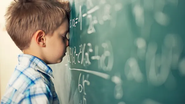 A young student has their eyes closed and is resting their head against a chalkboard full of math equations.