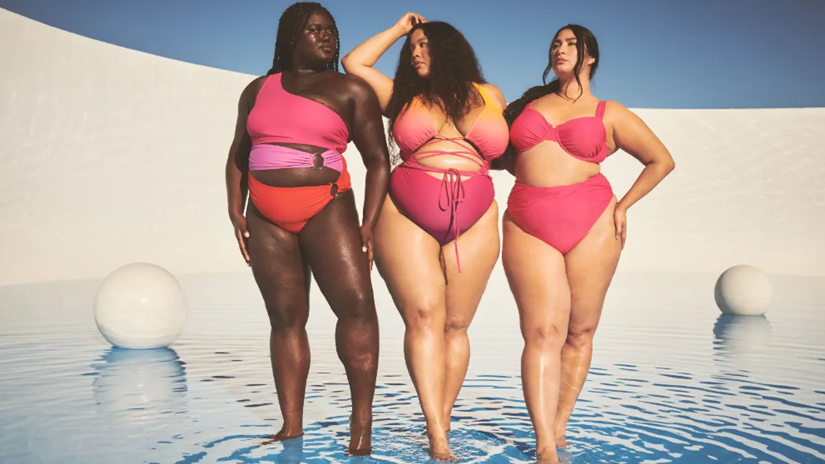 Three people in bathing suits that are brightly colored stand in a pool of water.