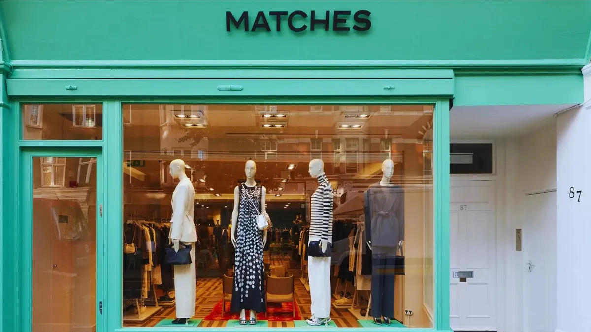 A green-trimmed store front of a Matches fashion store features mannequins in the window.