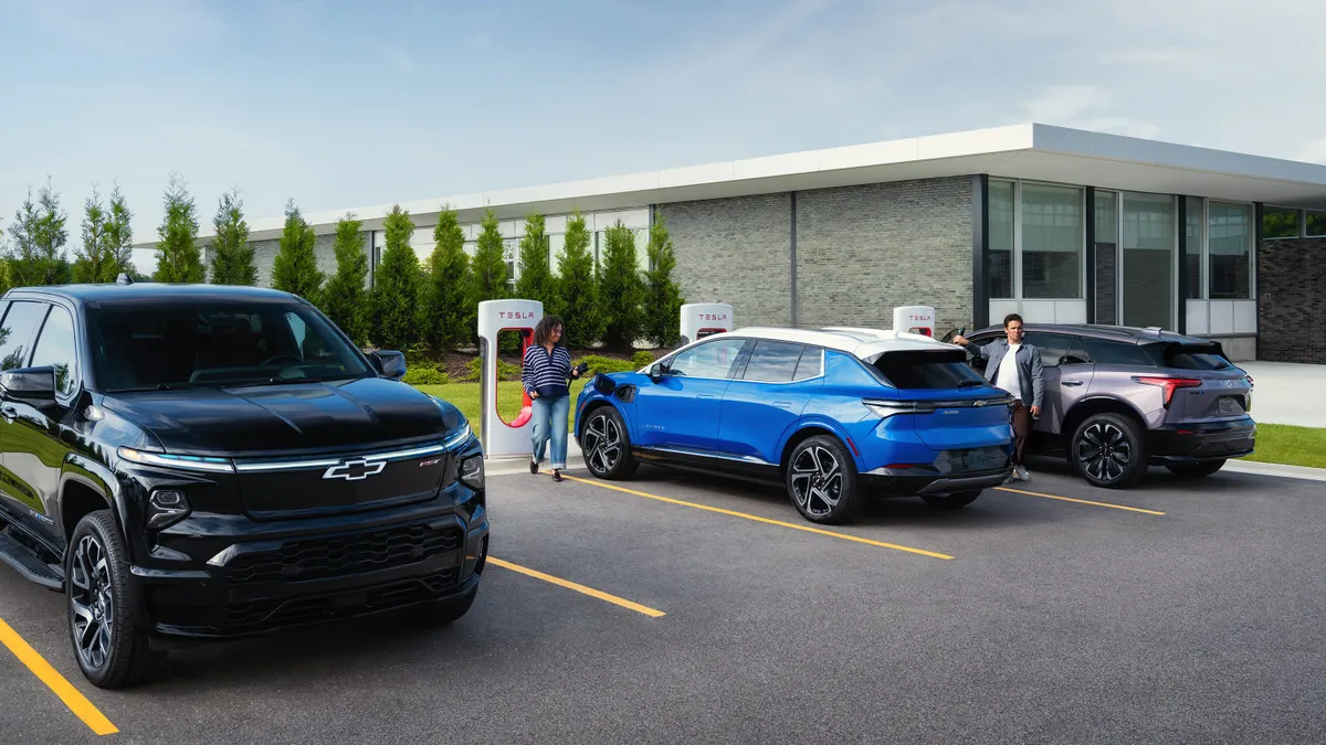 Three GM vehicles parked at a Tesla Supercharger location with a person preparing to plug in a blue Chevy Equinox EV.