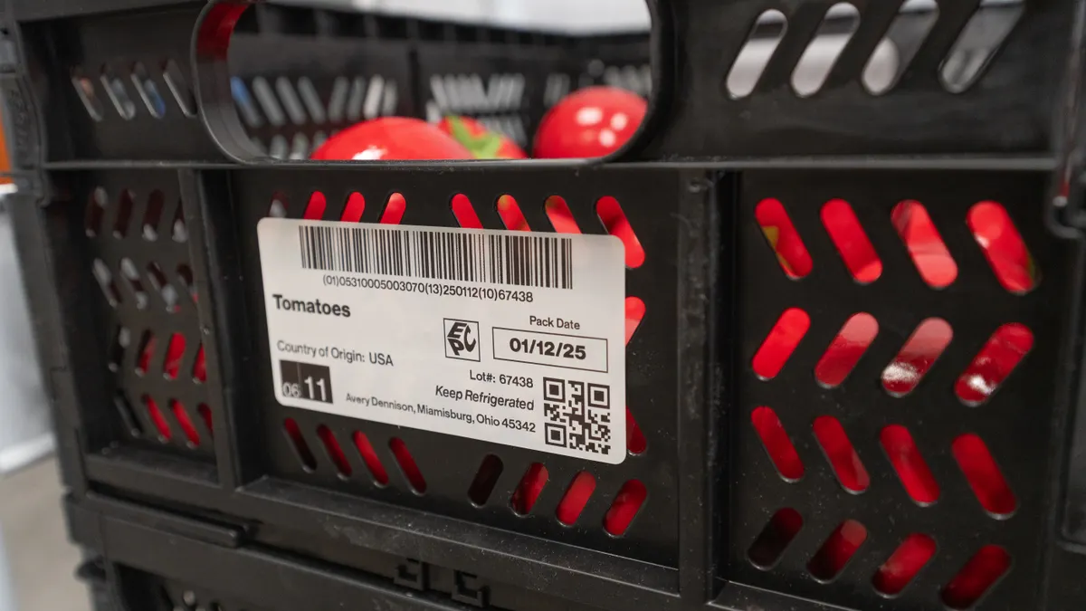 A black plastic crate filled with tomatoes has a label on the exterior indicating the contents.