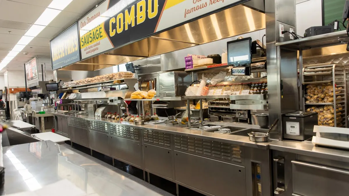 A empty kitchen inside a Portillo's restaurant that includes a makeline and some signage.