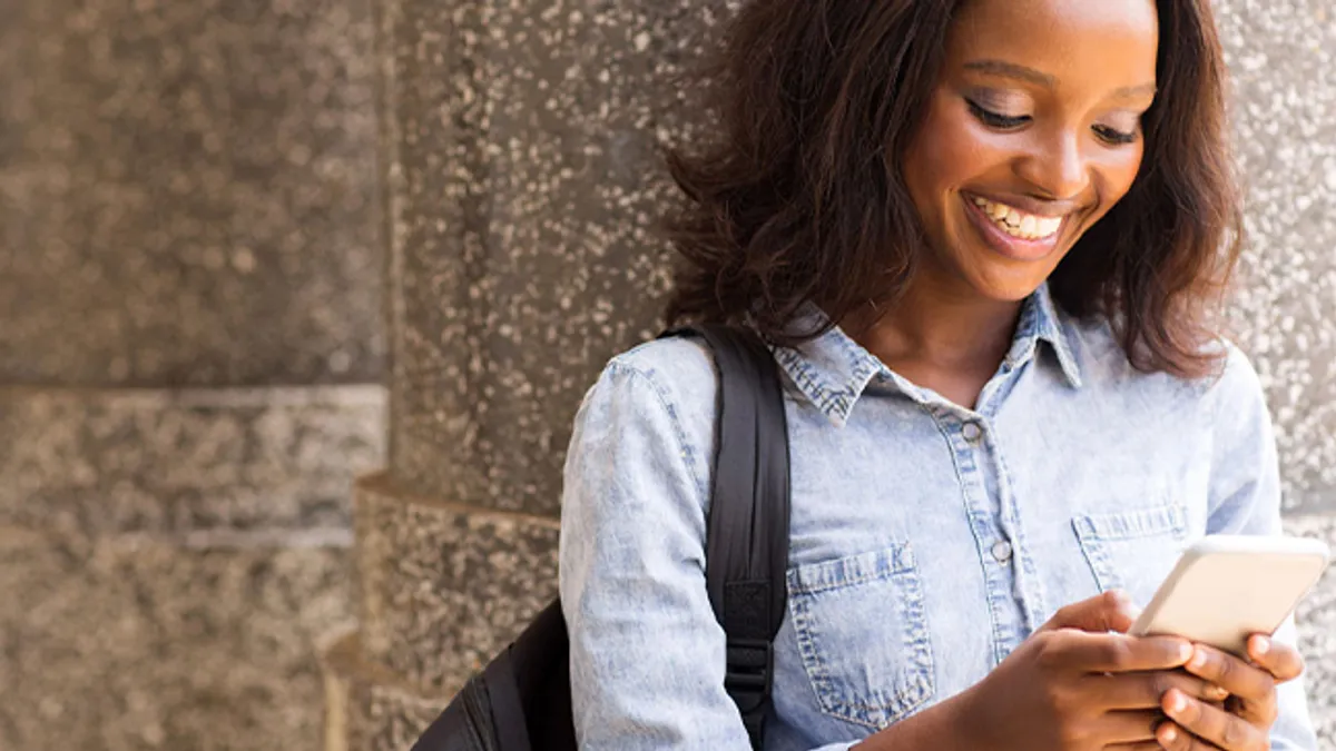 Happy afro american university student looking at phone.