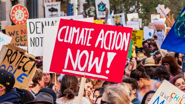 Many people hold signs that read "Climate Action Now" on an urban street. 