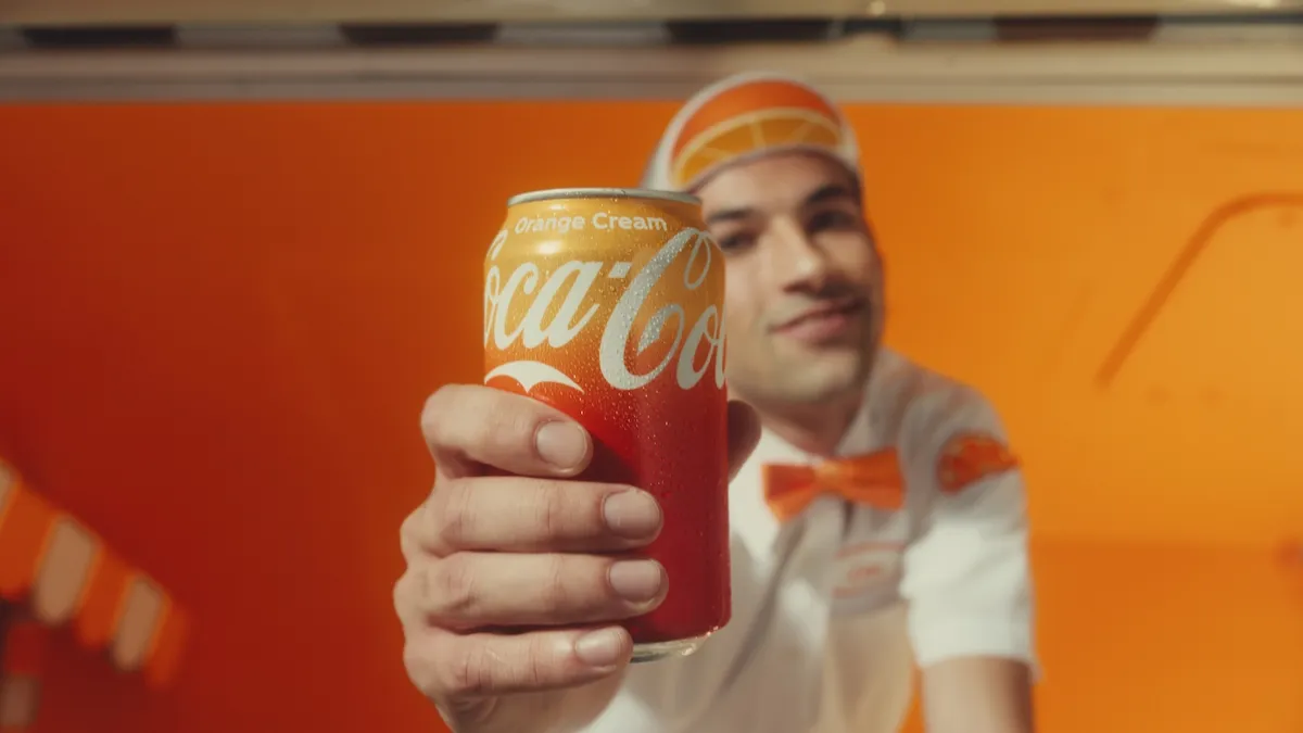 An ice cream truck driver hands out a can of Coca-Cola Orange Cream in an ad