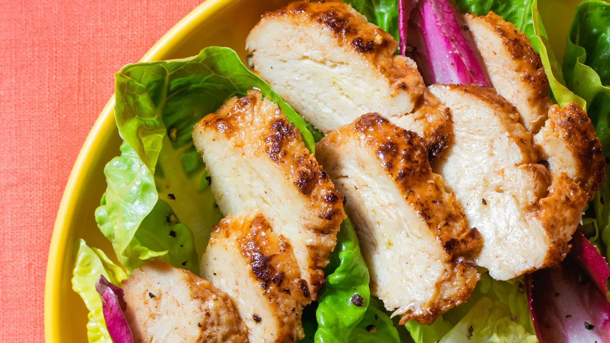 Bite-sized slices of cooked cultivated chicken from Upside Foods sit on a bed of greens.