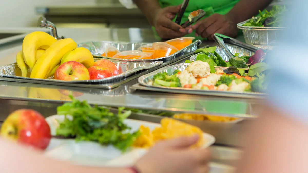 A high school student waits in line holding a tray of food before being served at a high school cafeteria.