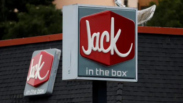 A photograph of a gray sign with a red box inside with white letters that says "Jack" under the box it says "in the box."