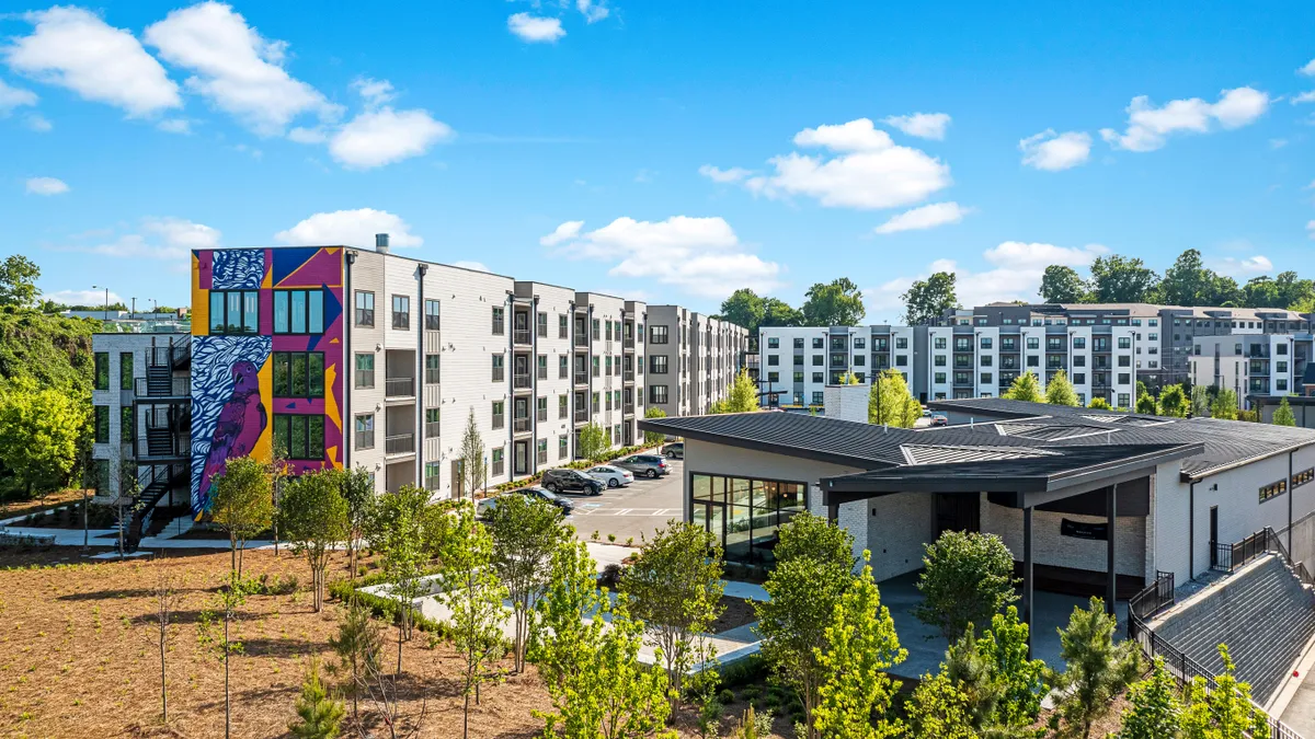 Modern, four-story apartment building with trees in the foreground.