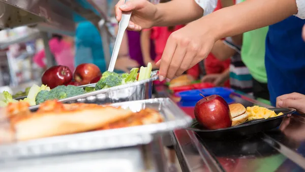 Cafeteria worker helping elementary students select food in lunch line