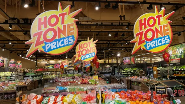 Three signs with the words "Hot Zone Prices" hanging above produce displays in a grocery store.
