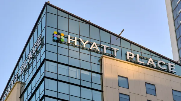 Corner view of a tall modern building with glass windows, beige panels, and the “HYATT PLACE” logo with colorful dots above.