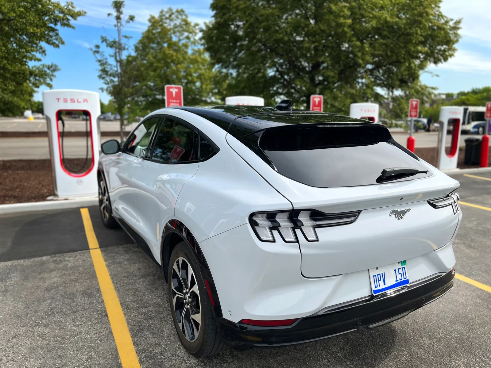 A Ford Mach E SUV parked in front of a Tesla Supercharger.