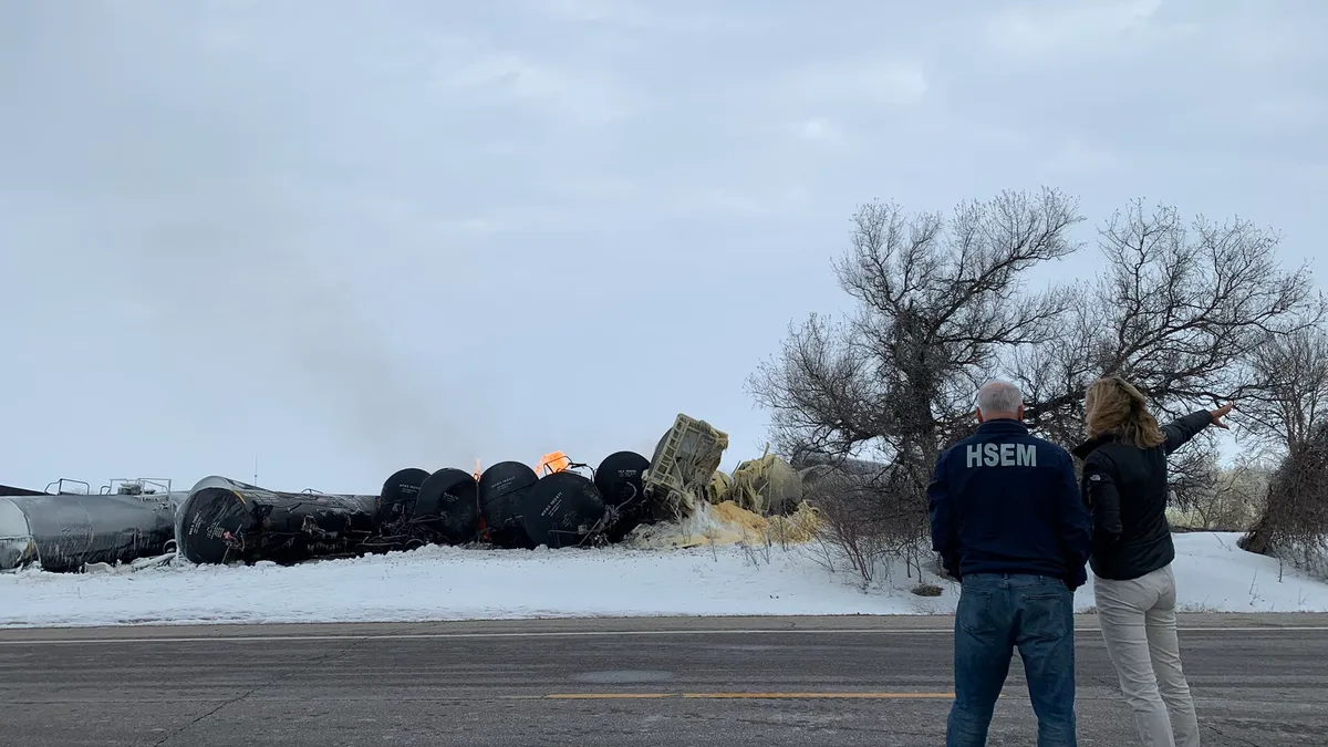 Image of two people with their backs to the camera looking at a train derailment.