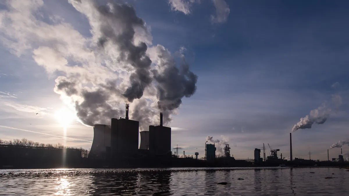 A factory is seen with a cloud of smoke behind it, demonstrating emissions.