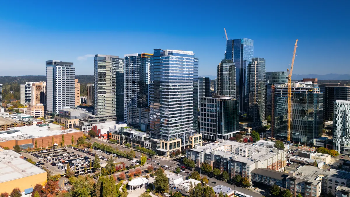 An aerial view of a city with high-rise buildings, cranes and a blue sky.
