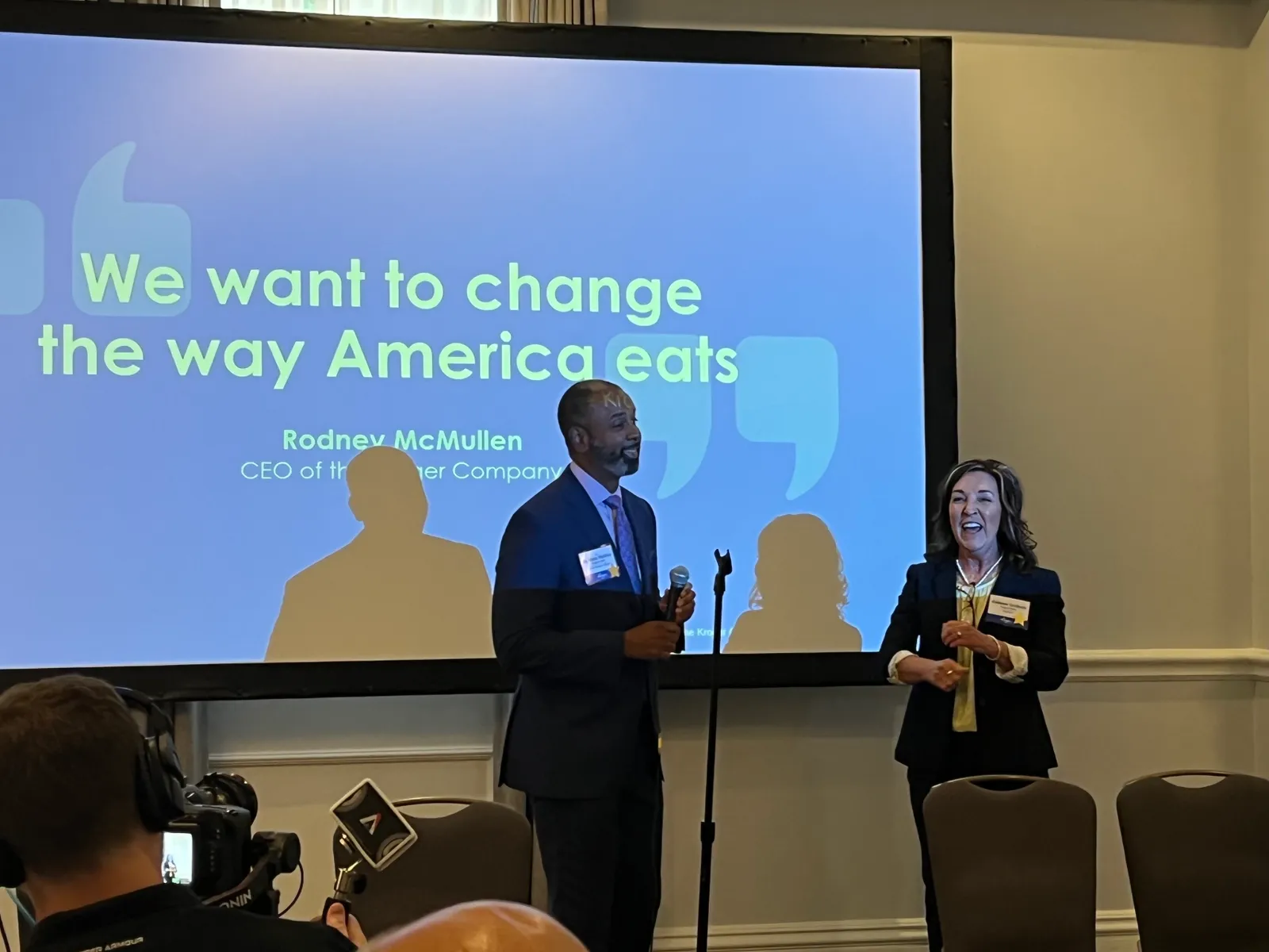 Two people speaking in front of a slideshow.