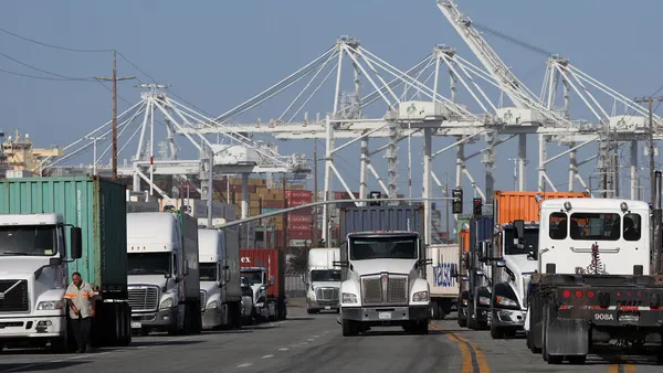 Trucks carrying shipping containers drive through an ocean port.