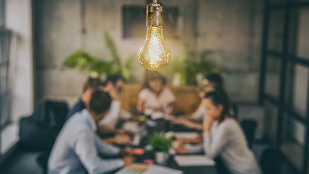 Several people sit around a table working with a lightbulb overhead.