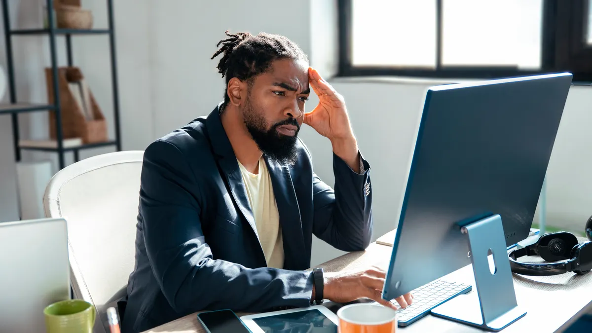 A man sits in front of a computer with a hand on his head.