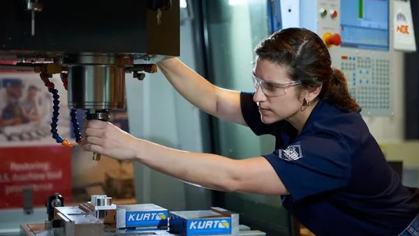 A person wearing protective goggles and their hair in a ponytail working on a machine.