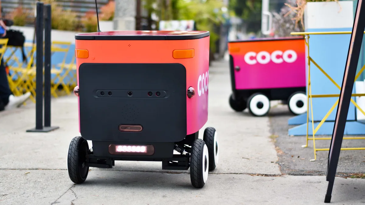 A Coco delivery robot travels along the sidewalk.