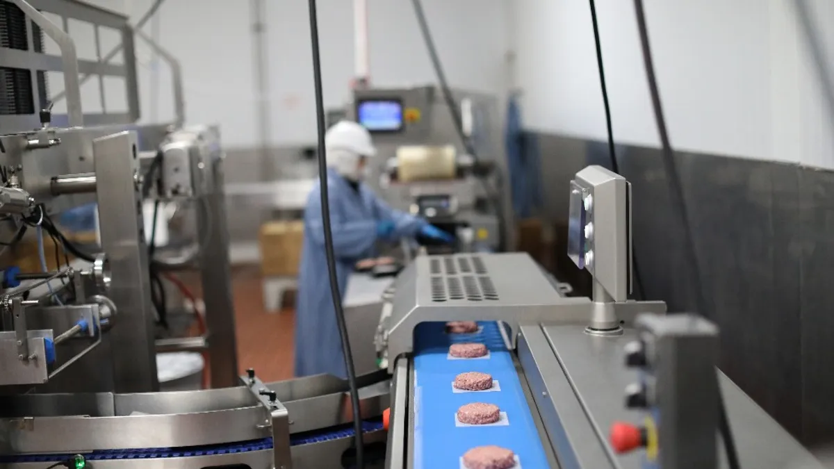 A worker stands in the distance as plant-based patties come down the line at a Beyond Meat factory