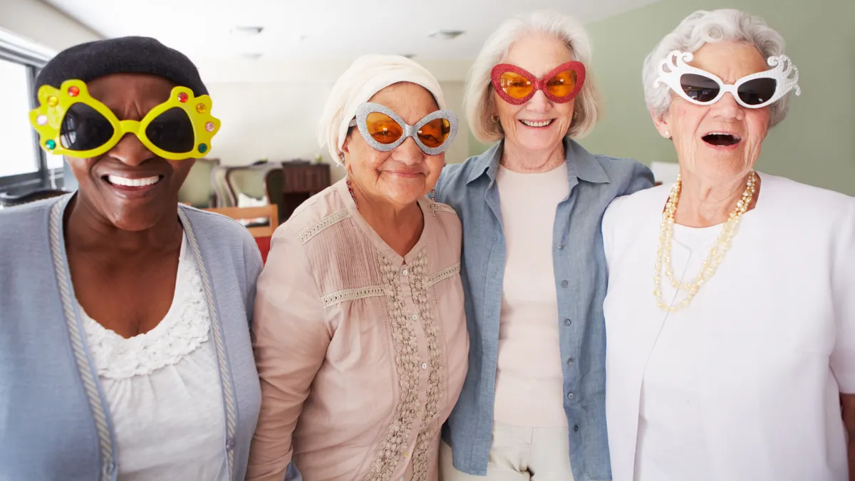 Four older people in oversized novelty sunglasses smile at the camera