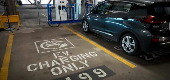 An empty EV charging station space next to a car charging in a parking garage