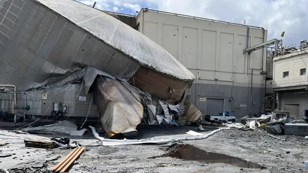 An exterior view of a collapsed industrial tank with a hole in the side surrounded by sandbags.