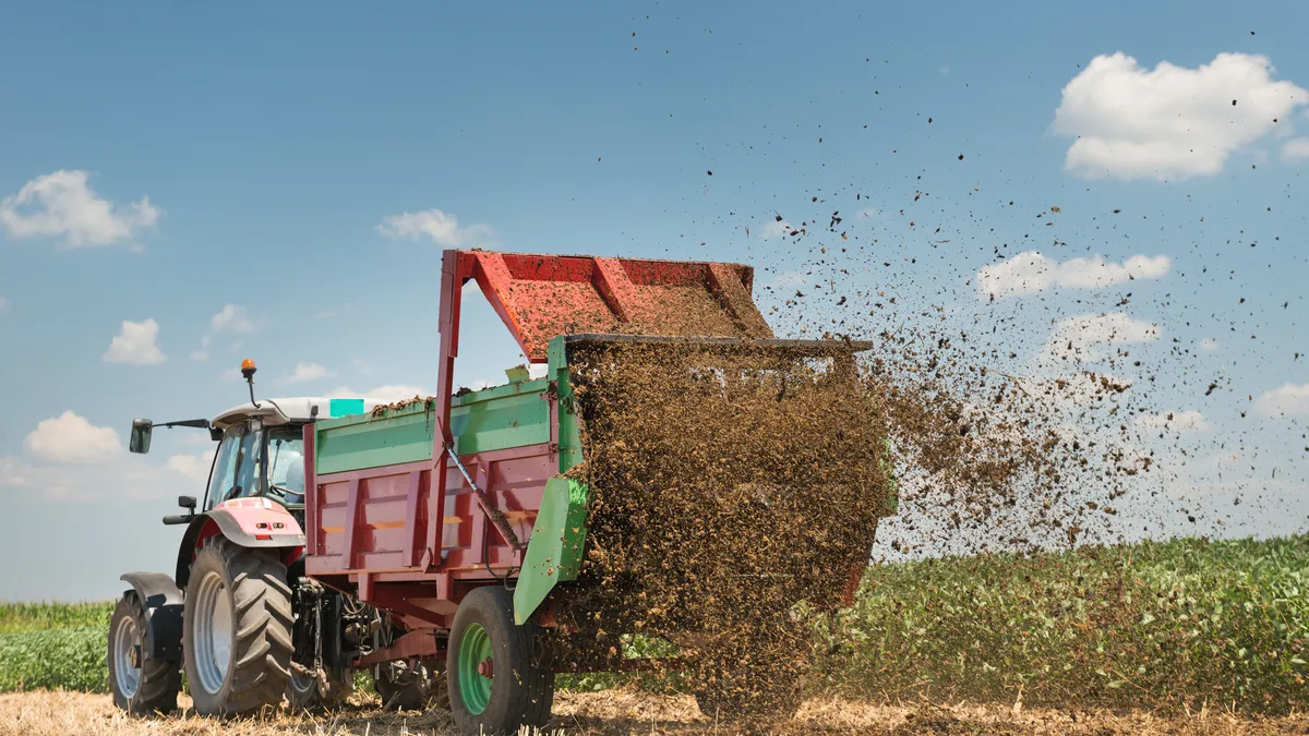 A tractor is seen spreading manure-based fertilizer on a field.