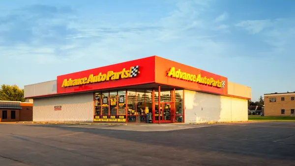 The exterior of an Advance Auto Parts store in a parking light with a blue sky above it.