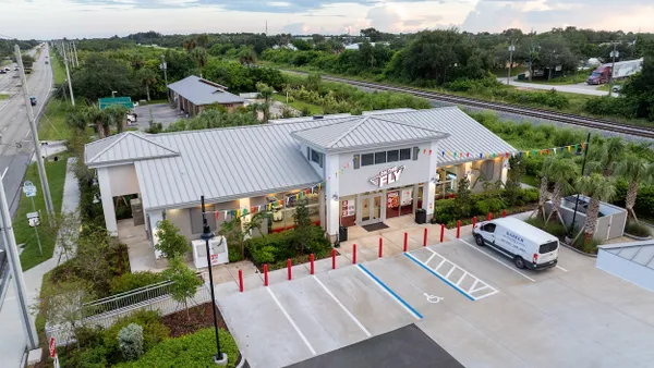 A photo of the exterior of a convenience store in Florida. The walls and roof are white, there are pennants from the building to two poles in the parking lot and there is a sign over the front door that reads "On the Fly."