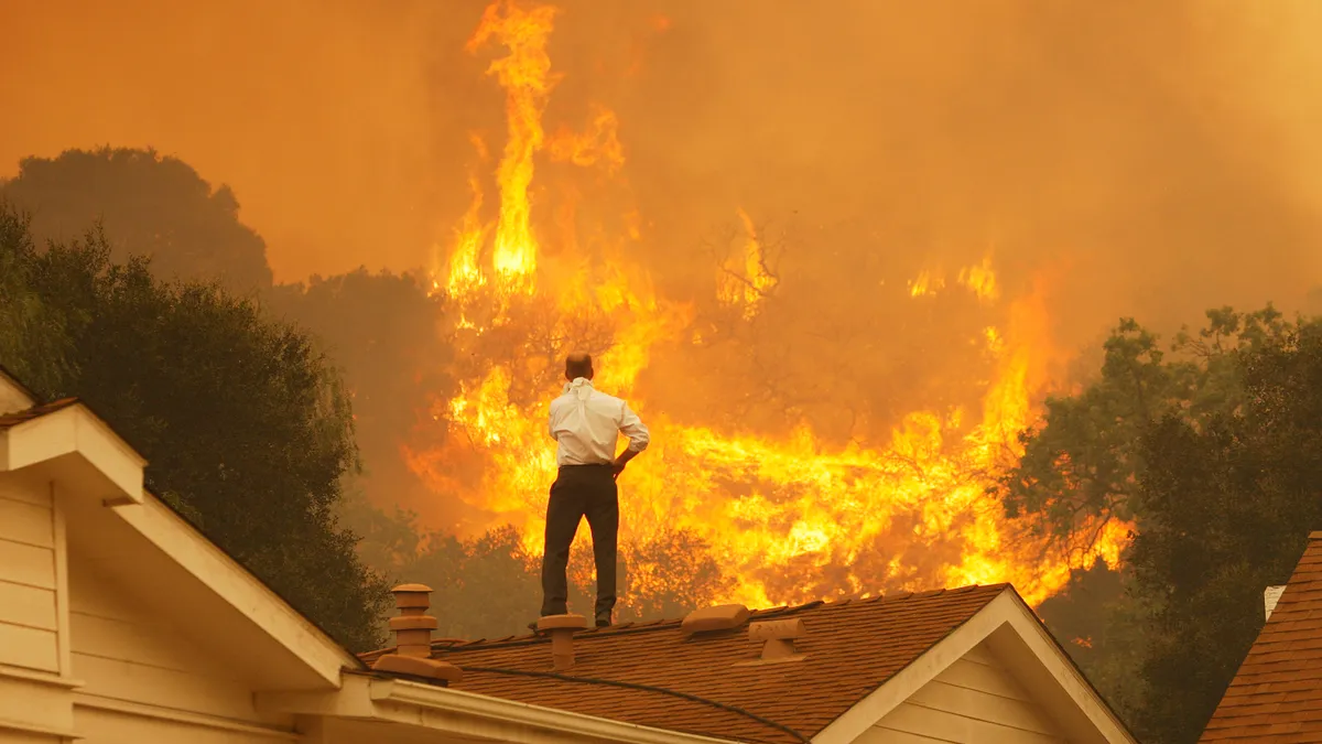 A man on a rooftop looks at approaching flames.