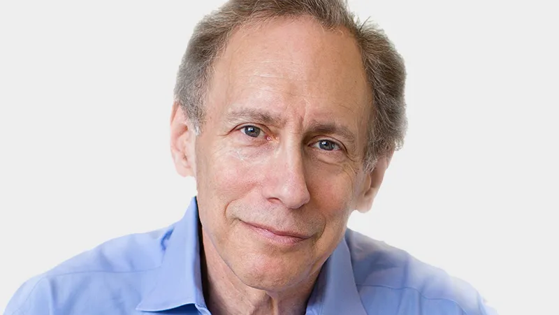 A man in a blue shirt looks into the camera for a headshot photograph.